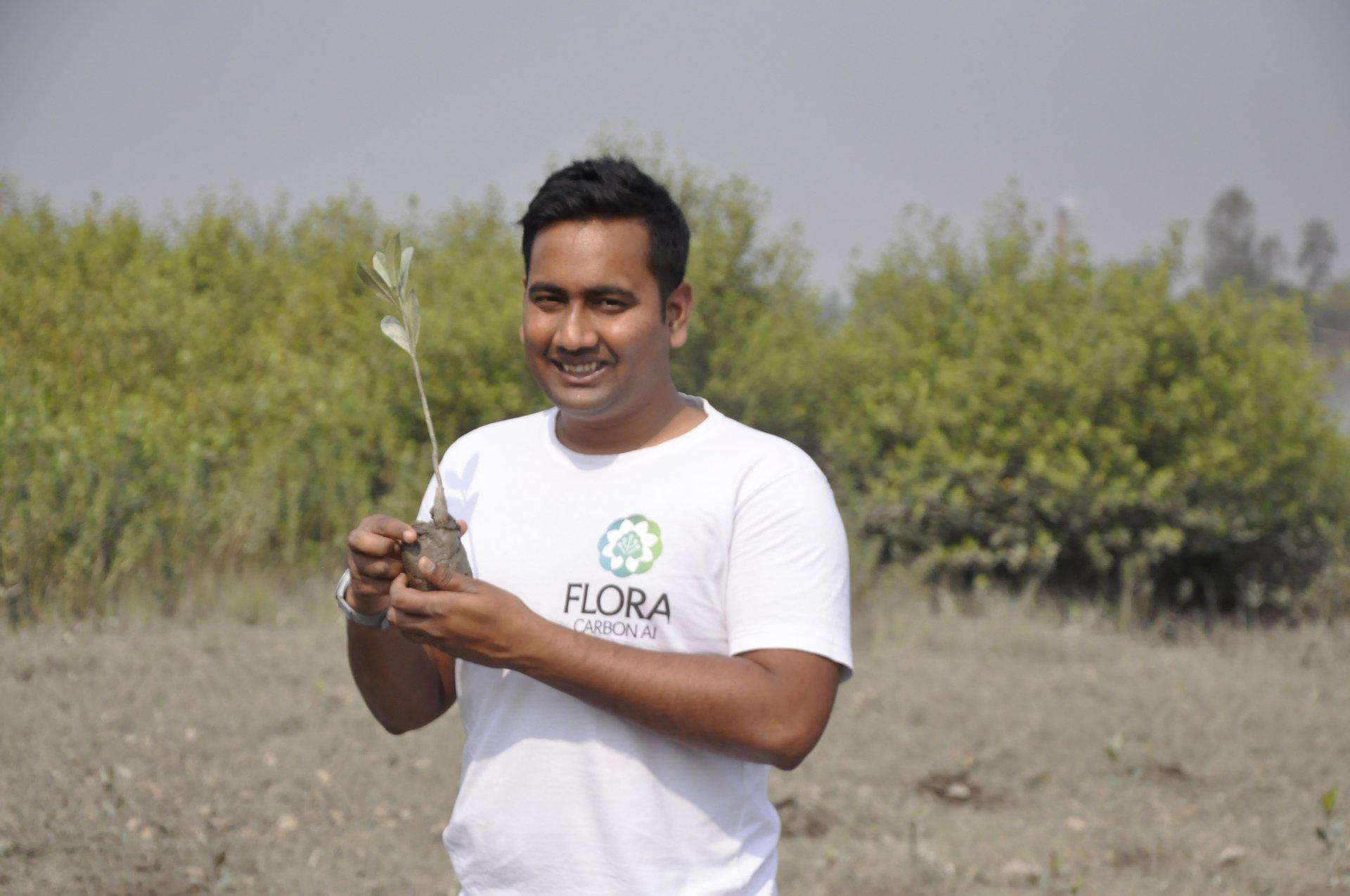 Manir Dhabak holding a sapling in the field, wearing a Flora Carbon AI t-shirt